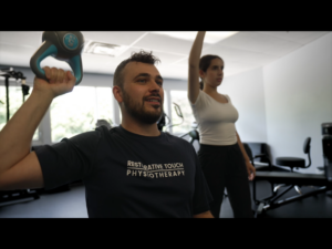 Athletic Therapist performing an overhead exercise demonstrating for a patient.