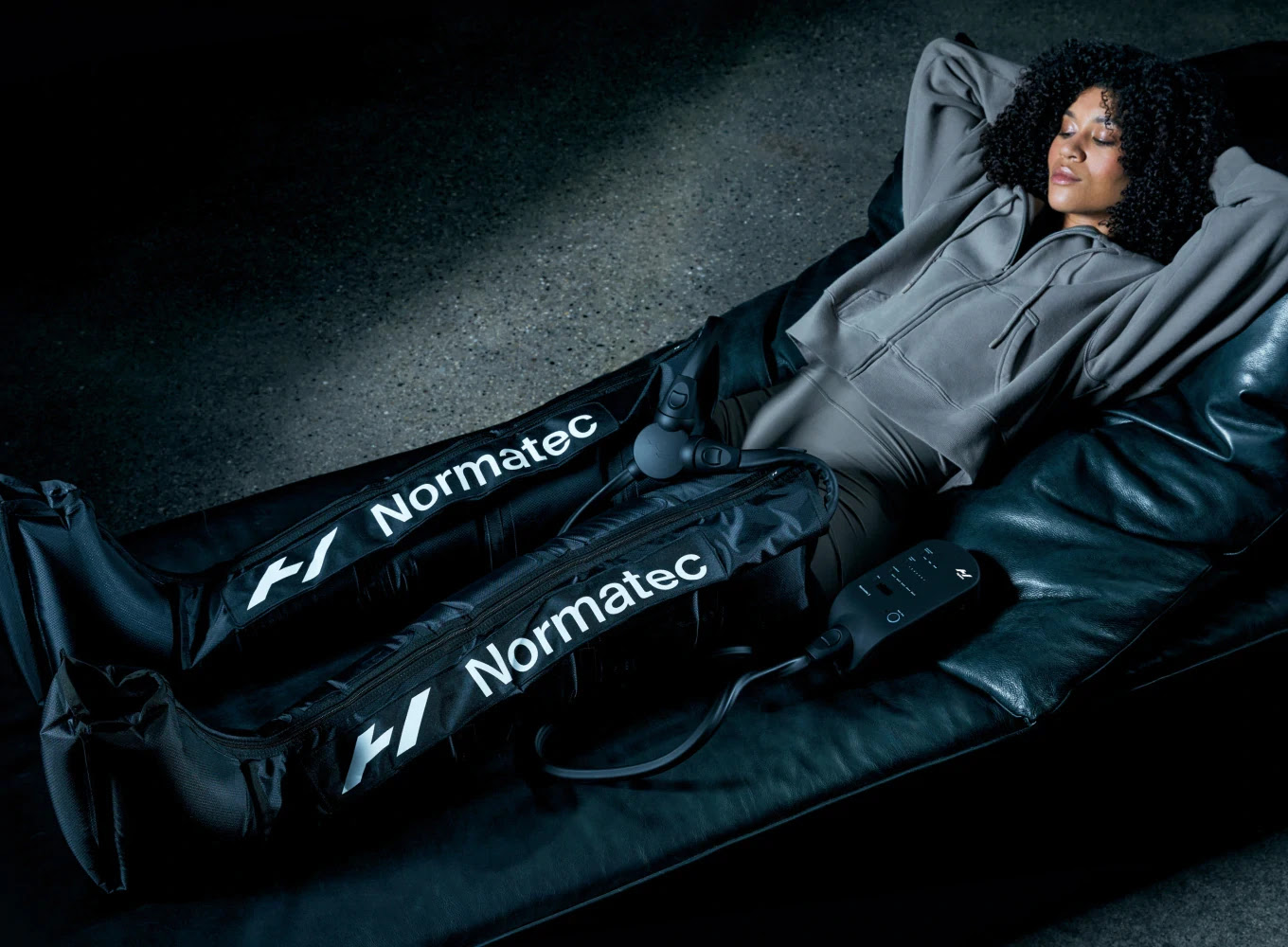 A woman lying on a mattress wearing NormaTec compression boots