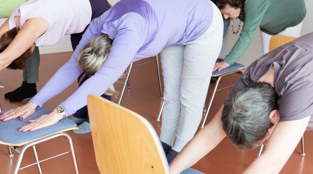 Active elderly folks stretching on chairs in colourful outfits